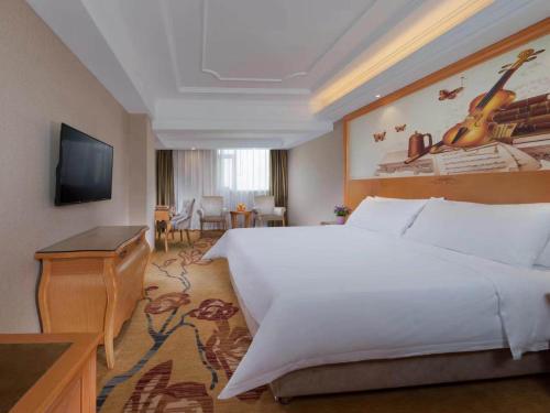 a bedroom with a large white bed and a television at Vienna International Hotel Shenzhen Longhua Xikeng Subway Station in Tiantangwei