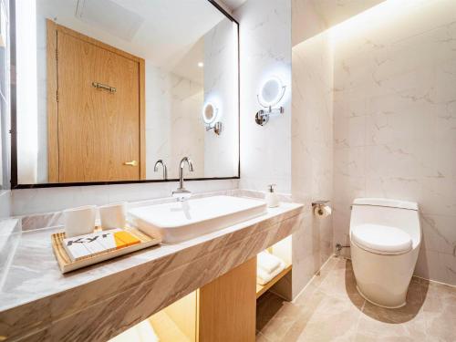 a bathroom with a sink and a toilet and a mirror at Kyriad Marvelous Hotel Heyuan Wanda Plaza in Heyuan