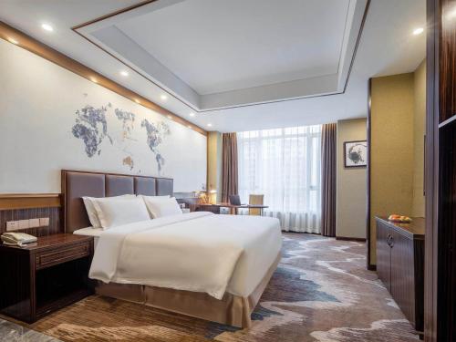 威海市にあるKyriad Marvelous Hotel Weihai Railway Stationの大きなベッドとデスクが備わるホテルルームです。