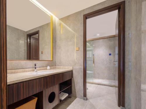 a bathroom with a sink and a mirror and a shower at Kyriad Marvelous Hotel Weihai Railway Station in Weihai