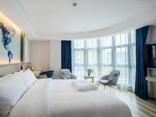 XiapuにあるKyriad Marvelous Hotel Fujian Xiapu Railway Stationの白い大型ベッドと椅子が備わるホテルルームです。