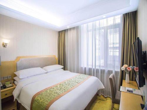 una camera d'albergo con letto, scrivania e finestra di Vienna Hotel Harbin Train Station Jianguo Street a Harbin