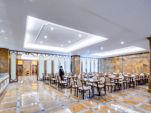 晋江市にあるVienna International Hotel Fujian Quanzhou Jinjiang Airportのテーブルと椅子の部屋に立つ男