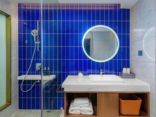 ein blau gefliestes Bad mit einem Waschbecken und einem Spiegel in der Unterkunft Kyriad Hotel Jiujiang Happy City in Jiujiang