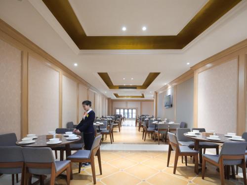 un homme debout dans une salle à manger avec des tables et des chaises dans l'établissement Vienna International Hotel Nanchang Qingshan Lake Wanda Plaza, à Nanchang