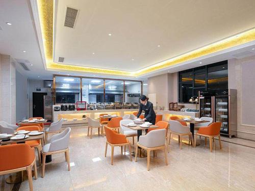 a man standing in a restaurant with tables and chairs at Vienna hotel Hunan Shaoyang Longhui Bus Station in Longhui