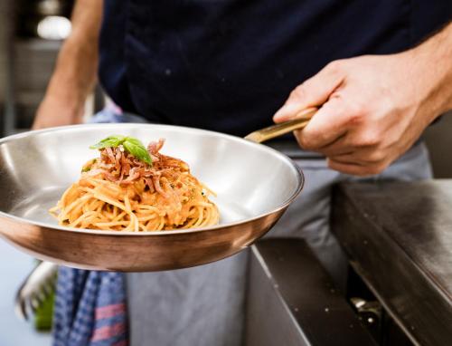 a person holding a bowl of spaghetti on a counter at Romantik Hotel Oberwirt in Marlengo