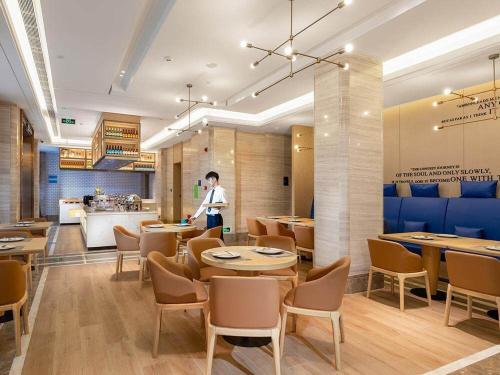 a person walking in a restaurant with tables and chairs at Kyriad Marvelous Hotel Shenzhen Nanlian Metro Station in Longgang