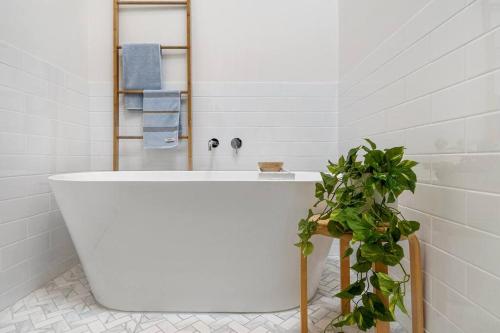 La salle de bains est pourvue d'une baignoire blanche et d'une plante. dans l'établissement Backbeach House - relaxing coastal escape, à Blairgowrie