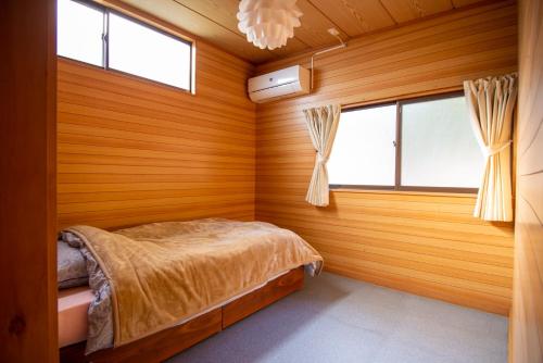 a bedroom with wooden walls and a bed and windows at Atelier&guesthouse ヌクリハウス in Ieyama