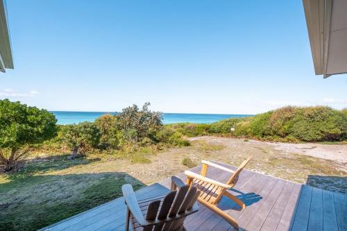 two chairs and a table on a deck with the ocean at Silver Moon at Half Moon in Bicheno