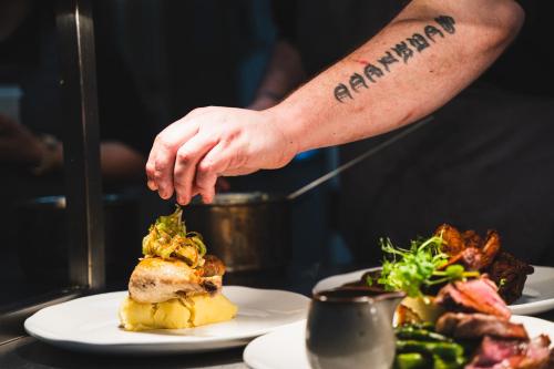 a man with a tattoo on his arm reaching for a plate of food at Kettleburgh Chequers in Kettleburgh