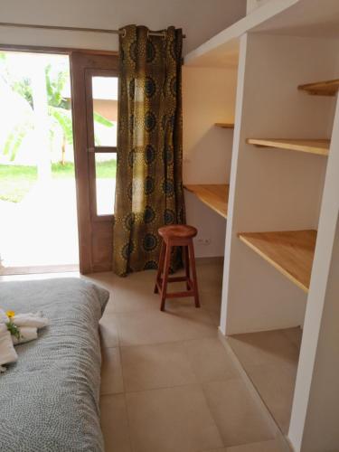 a room with a bed and a stool and a window at la maison de la fontaine in Cap Skirring