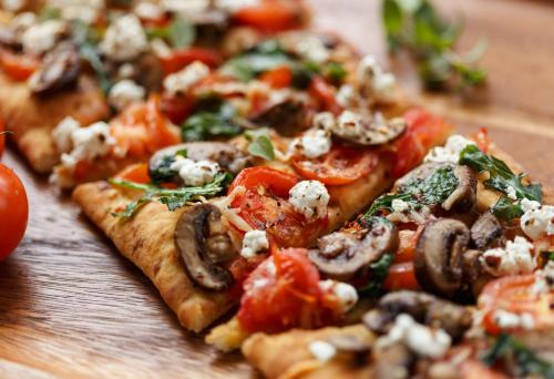 a pizza with tomatoes and mushrooms on a wooden table at Holiday Inn Jacksonville E 295 Baymeadows by IHG in Jacksonville