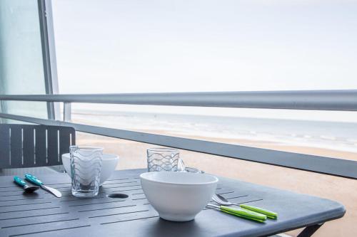 - une table avec des bols et des ustensiles sur le balcon dans l'établissement Les Marinas front of the beach, à Courseulles-sur-Mer