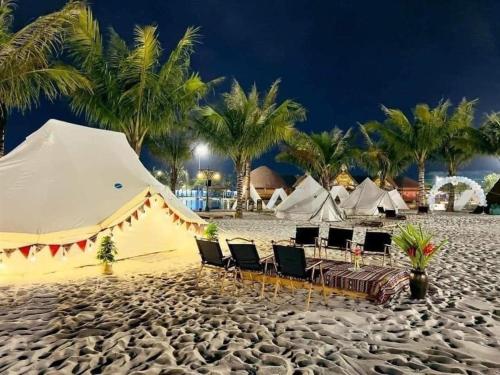 une tente et des chaises sur une plage de sable avec des palmiers dans l'établissement Lahomestay Chỗ Nghỉ 2PN Tiện Nghi, Khách Hàng Yêu Thích, à Tân Vạn