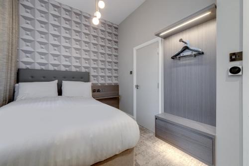 una camera con un letto bianco e una parete grigia di Mornington Victor Hotel London Belgravia a Londra