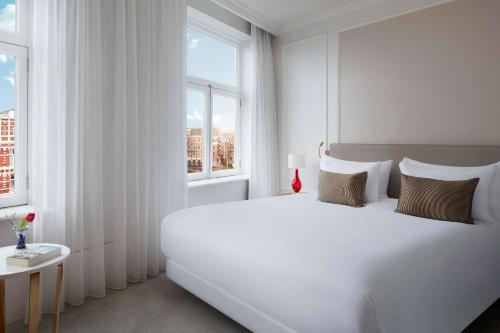 a white bedroom with a large white bed and a window at Tivoli Doelen Amsterdam Hotel in Amsterdam