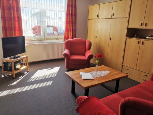 Una sala de estar con una silla roja y una mesa. en Kleines Logierhaus 03, en Norderney