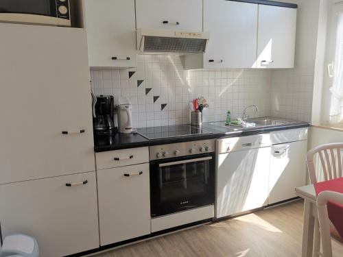 una cocina con armarios blancos y horno negro en Kleines Logierhaus 03, en Norderney