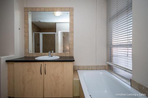 a bathroom with a tub and a sink and a mirror at 5A Sugar Beach with Inverter in Umdloti