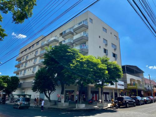 un edificio blanco alto con coches estacionados frente a él en Residencial Shalfa, en Foz do Iguaçu