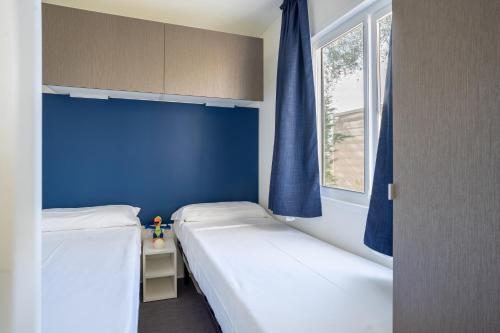 two beds in a room with blue walls and a window at La Rocca Camping Village in Bardolino
