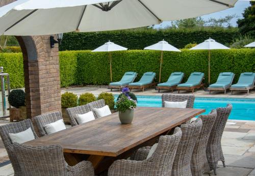 a wooden table with chairs and an umbrella at Hewas Water House - Private Pool, Hot Tub & Games Room in Grampound