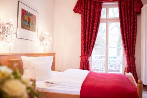 a bedroom with a bed with red curtains and a window at Hotel & Restaurant Grenzhof in Heidelberg