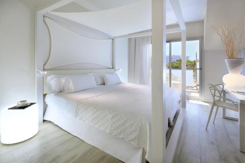 a white bedroom with a white canopy bed and a desk at Blanco Hotel Formentera in Es Pujols