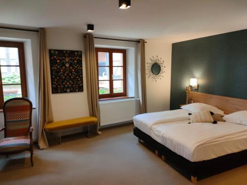 a bedroom with a bed and a chair and two windows at Hôtel le Saint Nicolas in Riquewihr