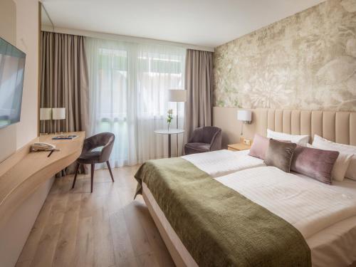 a hotel room with a large bed and a desk at Hotel Carbona Thermal Spa in Hévíz