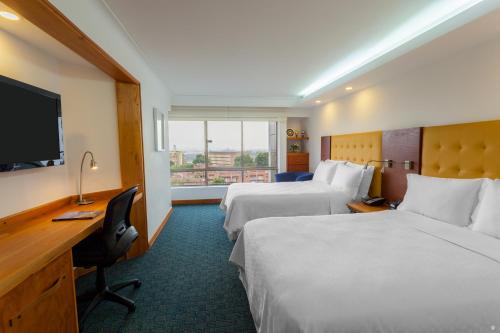 メデジンにあるFour Points by Sheraton Medellínのベッド2台、デスク、テレビが備わるホテルルームです。