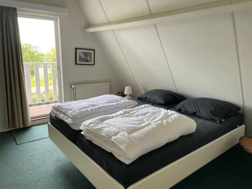 a bedroom with a large bed with white sheets and a window at Vakantiewoning Sneekermeer, huur sloep of zeilboot mogelijk in Goingarijp