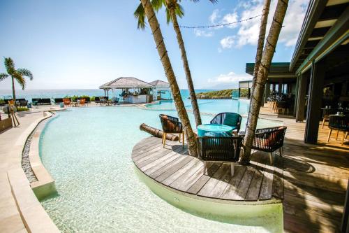 een zwembad met stoelen en een tafel naast de oceaan bij La Toubana Hotel & Spa in Sainte-Anne