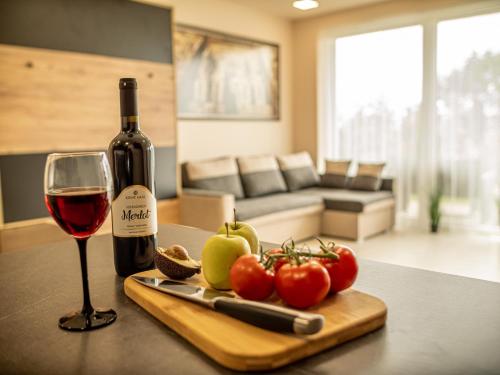 a bottle of wine and a cutting board with a glass of wine at Panorama Superior Apartments - Pool, garden, parking in Balatonalmádi