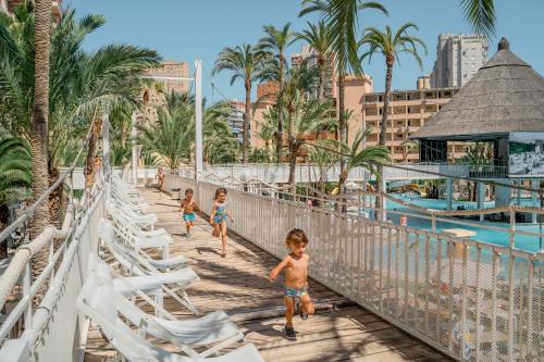 three children walking across a bridge over the pool at a resort at Magic Tropical Splash in Cala de Finestrat