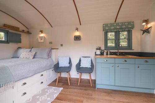 a bedroom with a bed and two chairs and a sink at Dipper's Hut - Luxury Shepherds Hut with Hot Tub in Blakeney