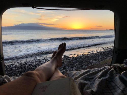 Campervan/Maui hosted by Go Camp Maui في كيهي: رجل يستلقي على شاطئ وقدمه على كتاب
