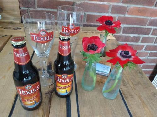 three bottles of beer on a table with flowers and glasses at Tiny home Texel in Den Burg