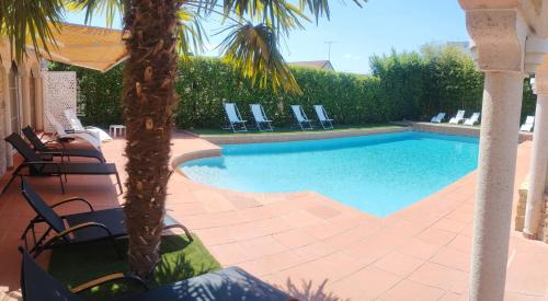 a swimming pool with chairs and a palm tree at Le Mas Champenois in Châlons-en-Champagne