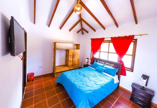 1 dormitorio con 1 cama azul y TV de pantalla plana en cabaña villa rica, en Ráquira