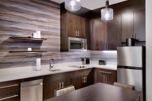 Residence Inn by Marriott Brunswick في برونزويك: مطبخ مع دواليب خشبية وثلاجة حديد قابلة للصدأ