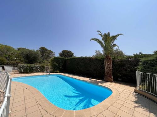 une piscine bleue avec un palmier et une clôture dans l'établissement Charmant T2/Mezzanine avec Piscine et Terrasse, à 5 min de la Plage, St-Raphaël - FR-1-226A-148, à Boulouris-sur-Mer