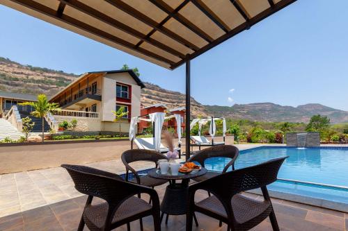 a table with chairs next to a swimming pool at Asanjo Villa by VEO - Part of StayVista in Mulshi