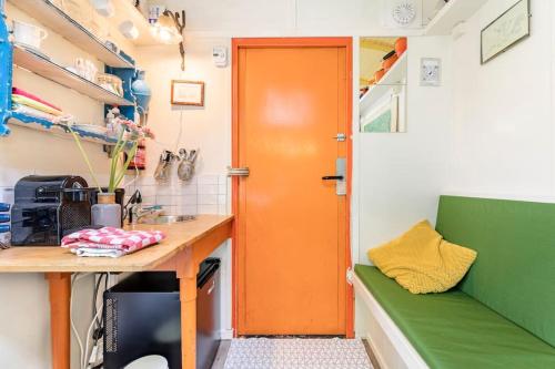 uma porta laranja numa cozinha com uma secretária e um banco verde em Tiny House em Kampen