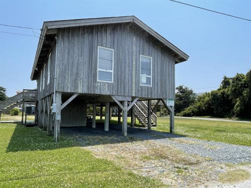Un pequeño edificio de madera con una escalera en un campo. en Gray Eagle House 58202, en Hatteras