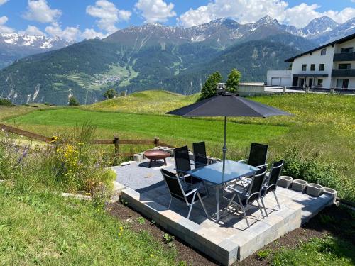 einen Tisch mit Stühlen und einem Sonnenschirm auf einer Terrasse mit Bergen in der Unterkunft Alpenglück in Fiss