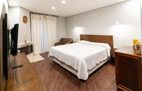 um quarto com uma cama branca e uma televisão em Flat 5 estrelas em Campos do Jordão em Campos de Jordão