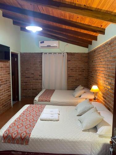 a bedroom with two beds and a brick wall at Hotel Yvy Pyta in San Ignacio